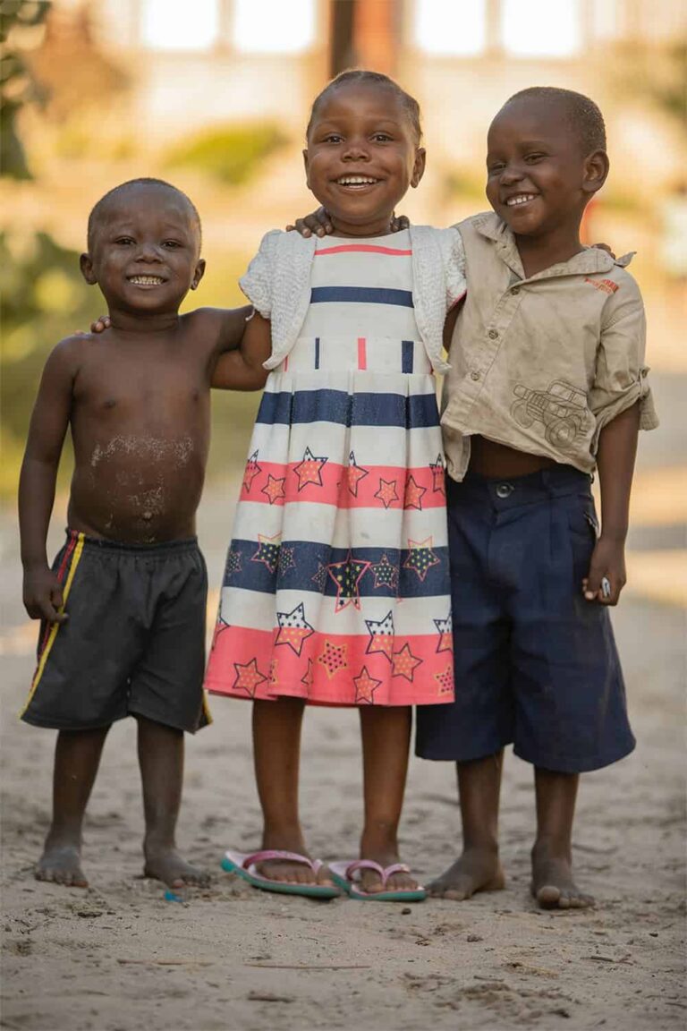 Three smiling children standing together outdoors